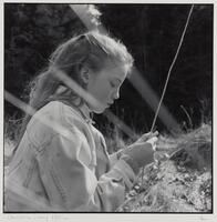 Side view of a girl in a field holding a thin stick in her hand. She is wearing a denim jacket.