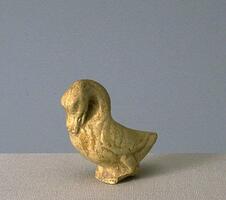 A small earthenware figure of a duck standing on two feet with head curved down, covered in a straw-colored glaze.