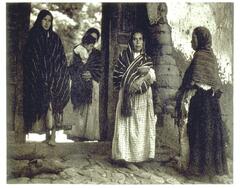 This is a photograph of a group of women standing around a doorway. Four women stand, one holding an infant child, another holding a baby beneath her shawl.