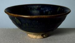 A bowl on a straight foot ring and subtle rim eversion, covered in a thickly applied, iron-rich black glaze with lighter russet-brown partridge feather markings (鷓鴣斑), <em>zhegu ban</em>. The thick glaze thins at the rim to a russet-brown color.