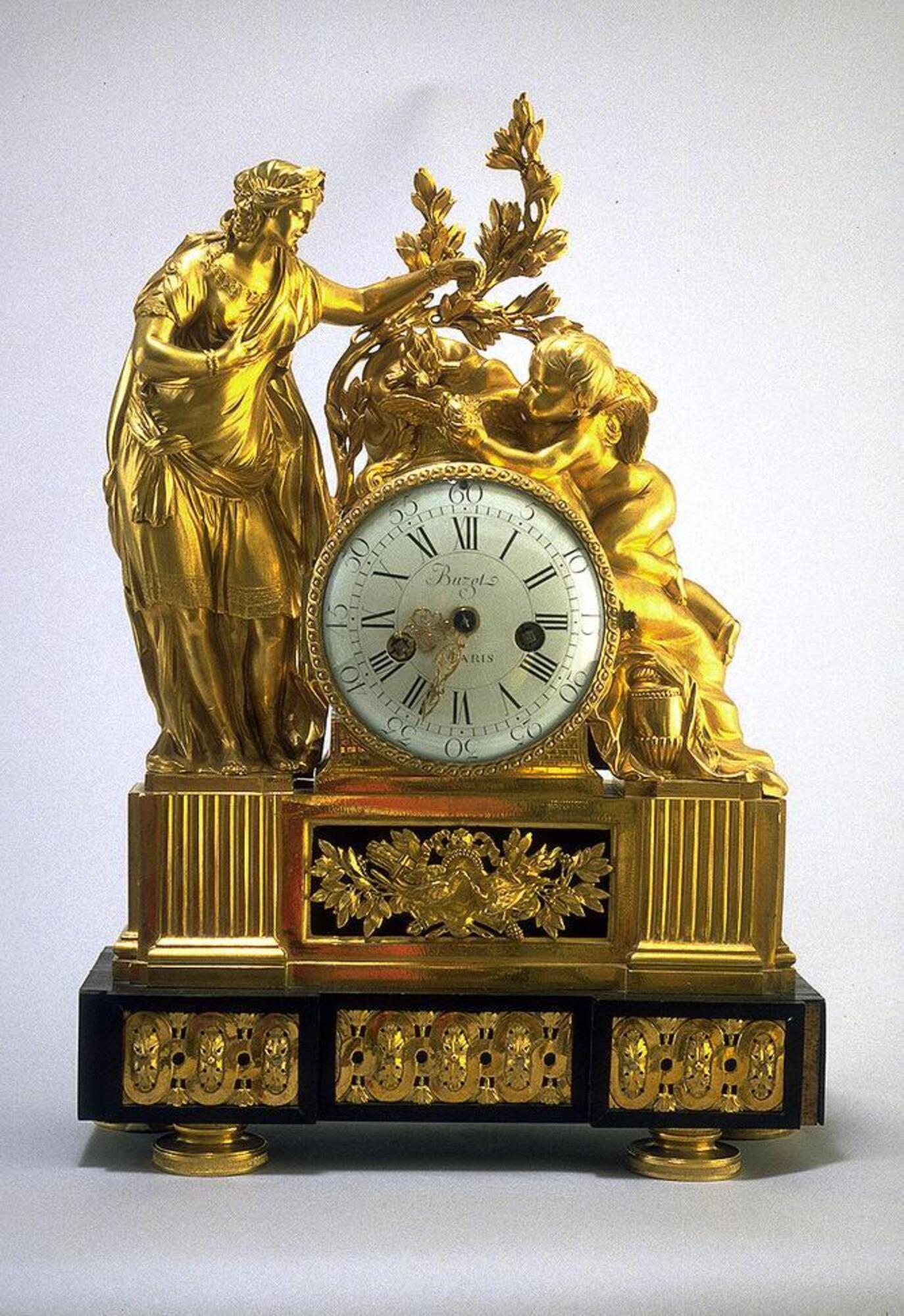 The dial of this elaborately decorated clock stands upon a two-tiered base. The lower tier consists of a hollow base made of ebony and adorned with a frieze of gilded bronze scrollwork and palmette motifs. The upper tier, made entirely of gilded bronze, features six fluted pilasters with a decorative panel centered on the front below the dial. This panel is composed of a pair of doves touching beaks before a crossed quiver of arrows and a flaming torch framed by leaves. A woman in long flowing robes stands to the right of the dial and empties a small cup onto a dove held by a winged putto who lies on a rocky projection. Behind the dove burns a fire on a small altar inscribed "Altar of Venus" [Autel à Venus].