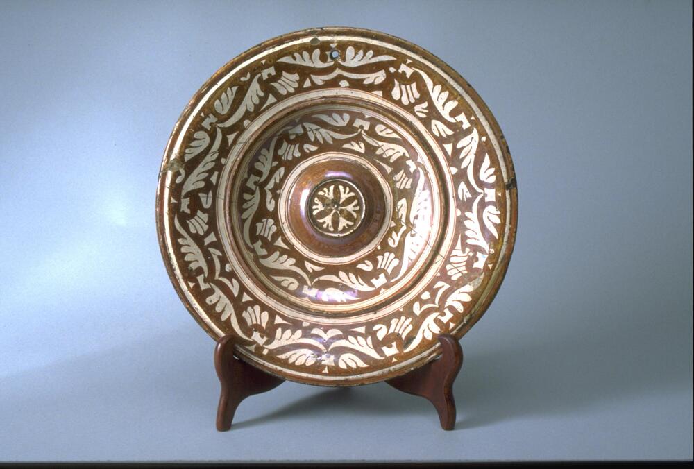 This dish features a recessed center with a central boss decorated with a rosette design. The recessed area and rim are painted with floral motifs and leaf designs arranged in concentric rings.