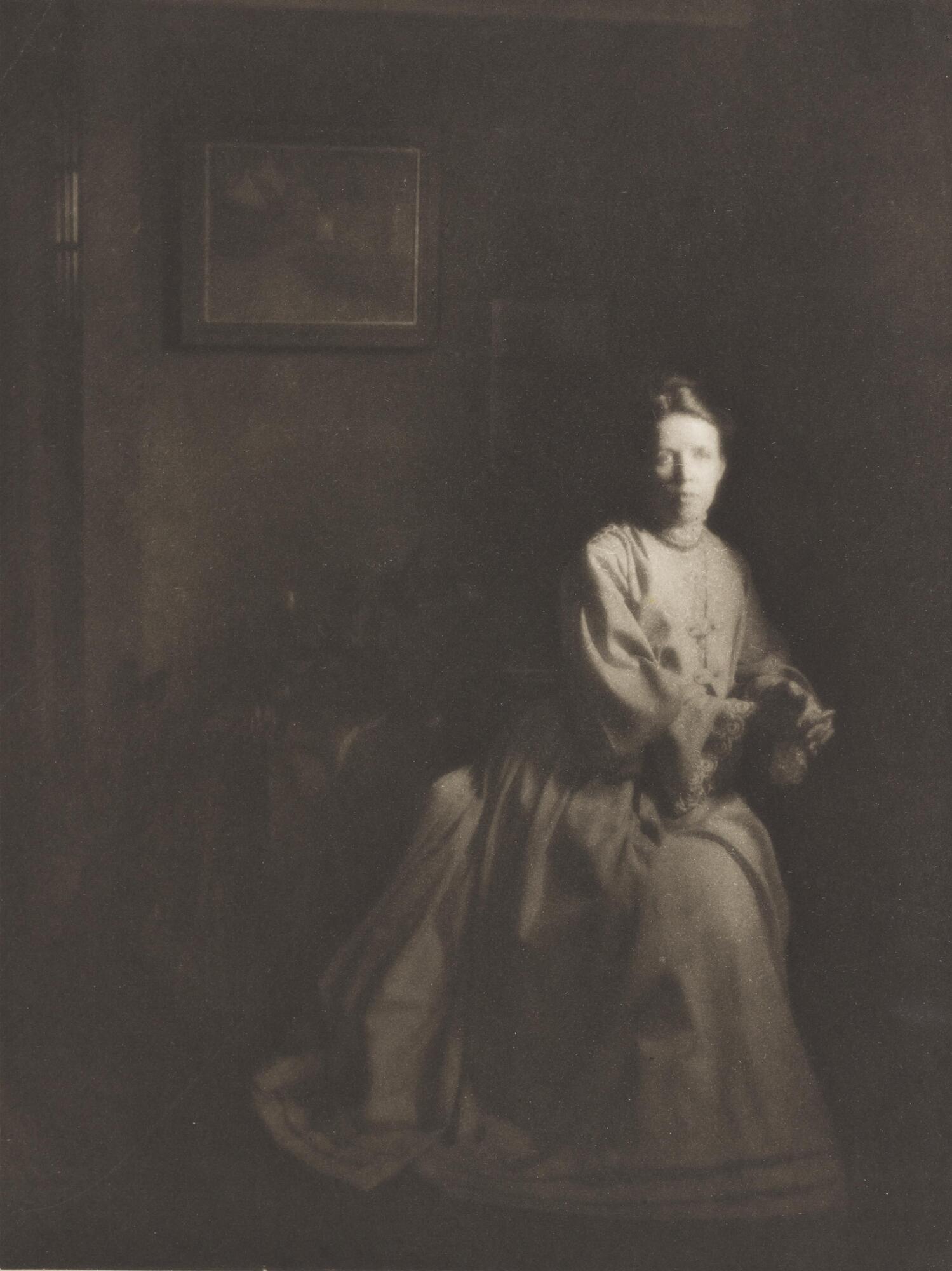 Portrait of a woman in a darkened interior space, seated next to a window.
