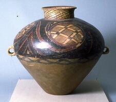 This light reddish-buff earthenware <em>guan (</em>罐) jar has a wide globular upper body and conical lower body on a narrow flat base with a tall narrow neck and flaring rim. There are two diametrically opposed lug handles at the waist. Painted on the upper half of the body with black and red pigments are four whirls containing a network pattern within larger diamond shapes, confined between solid band borders, with a lobed line border below. Around the neck is a cross-hatched network design, hatch marks and solid bands to the interior.  