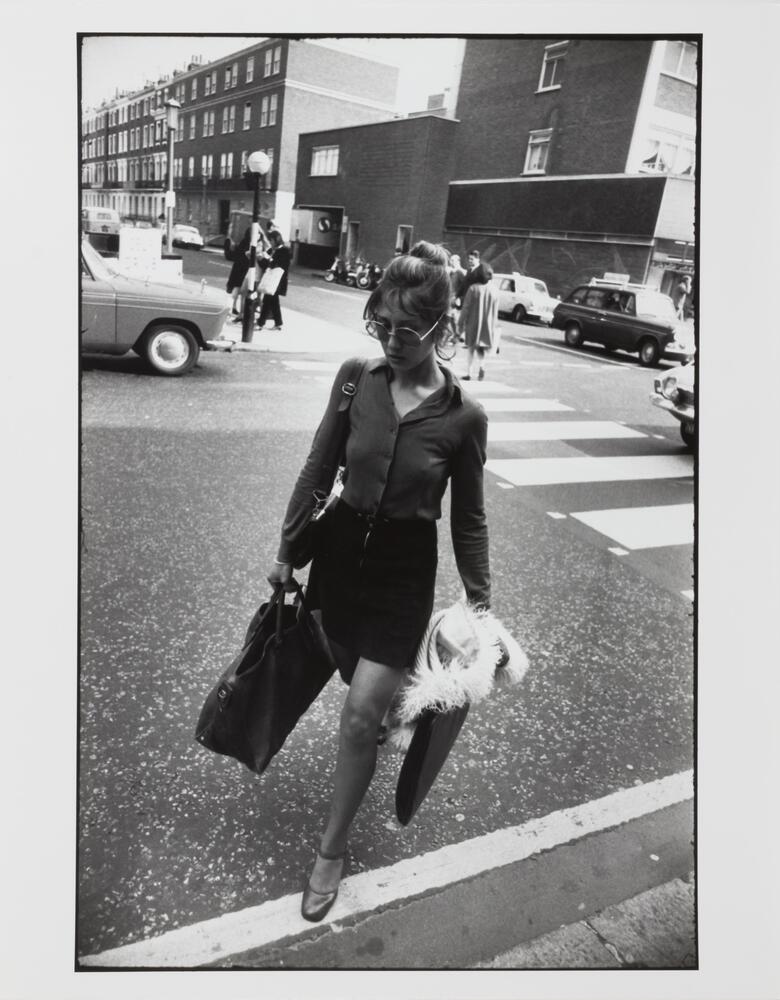 Photograph of a woman crossing a busy street, her path straying from the designated crosswalk visible in the background.