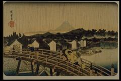 Vertical lines stream downward across the print indicate torrents of rain. Several travelers with umbrallas and straw hats are walking across the bridge over the river. A village alongside the river and mountains are shown in the background.