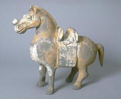 An earthenware model of a stocky horse on short legs, dressed in a saddle blanket and saddle with a roundel on its nose, a short downward pointing tail and trimmed mane, and traces of mineral pigment. 