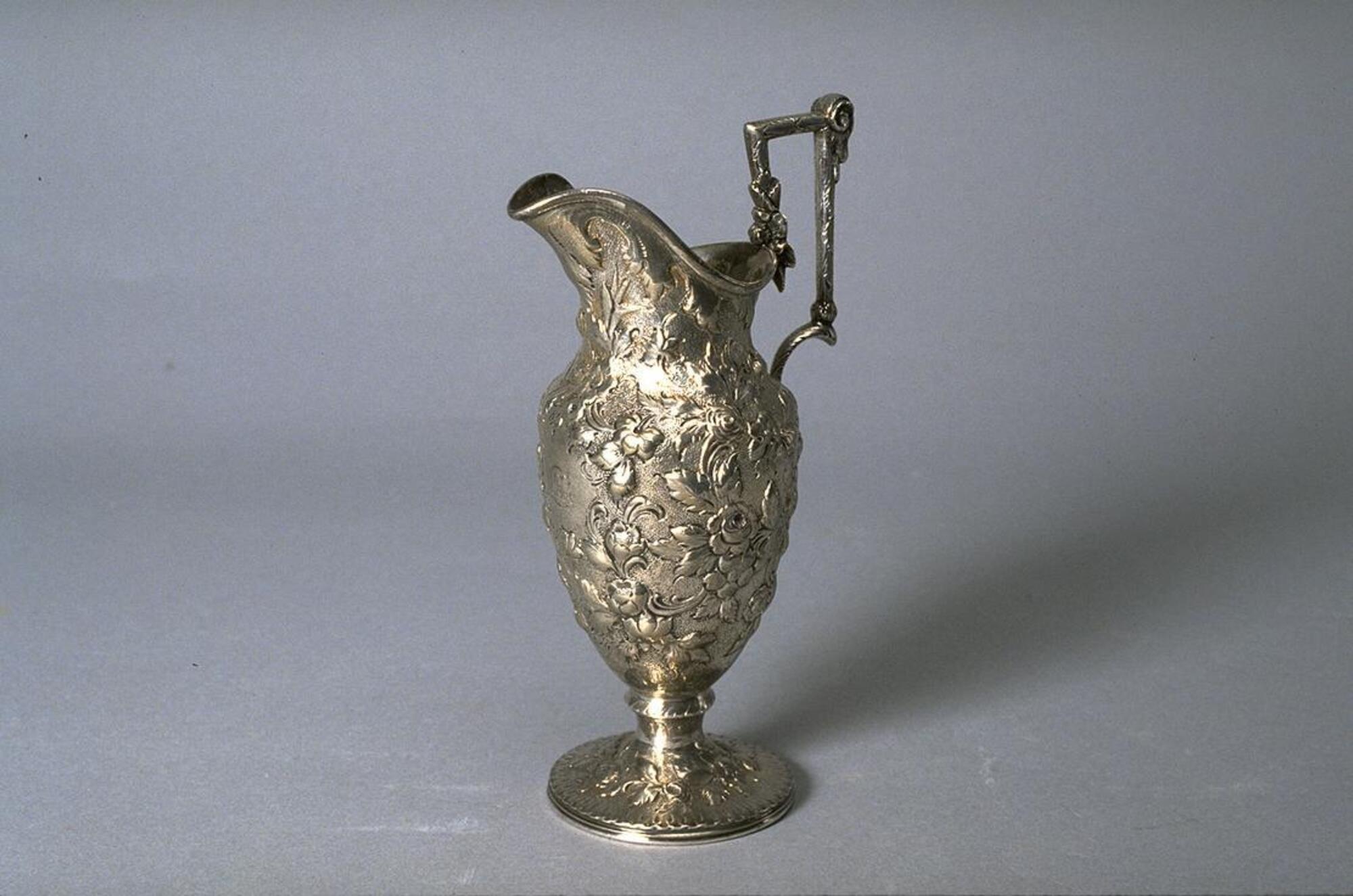 Pitcher-shaped silver vessel with square handle and opulent repouss&eacute; decoration