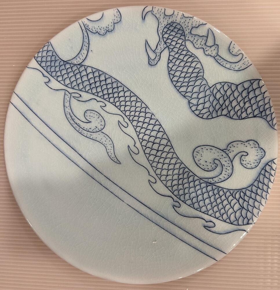 This plate is a border element of the piece with two blue, curved lines below a blue dragon&#39;s tail with scales and a wavy, fin-like edge. The dragon&#39;s paw and three claws are visible in the top of the piece.&nbsp;