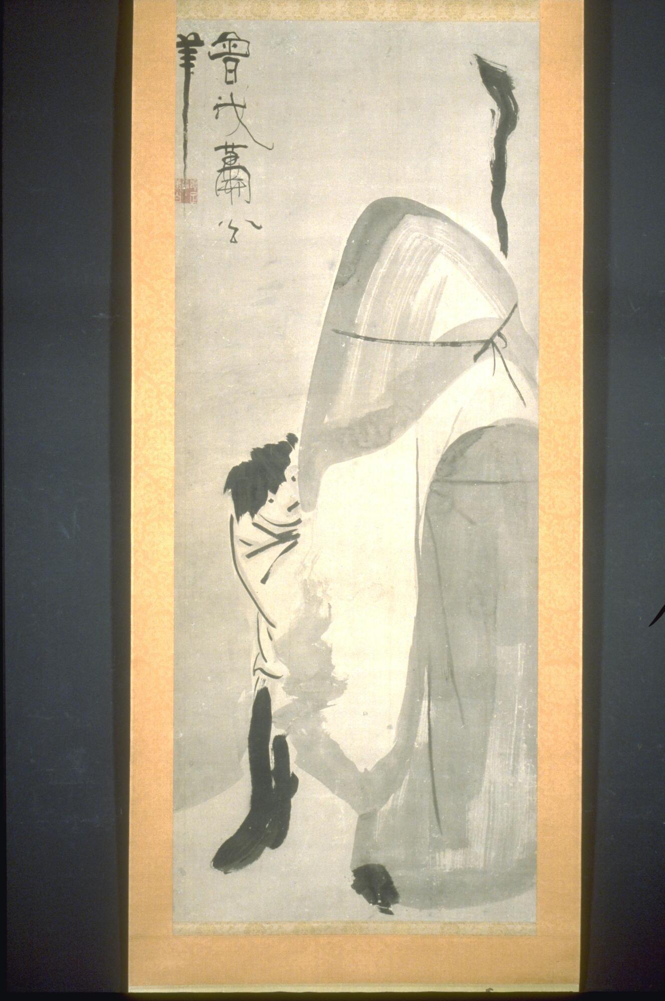 This hanging scroll depicts two figures, one with with a head covering and billowing robes holding a staff, and a shorter figure looking out towards the viewer. An inscription is placed in the upper left corner of the image.