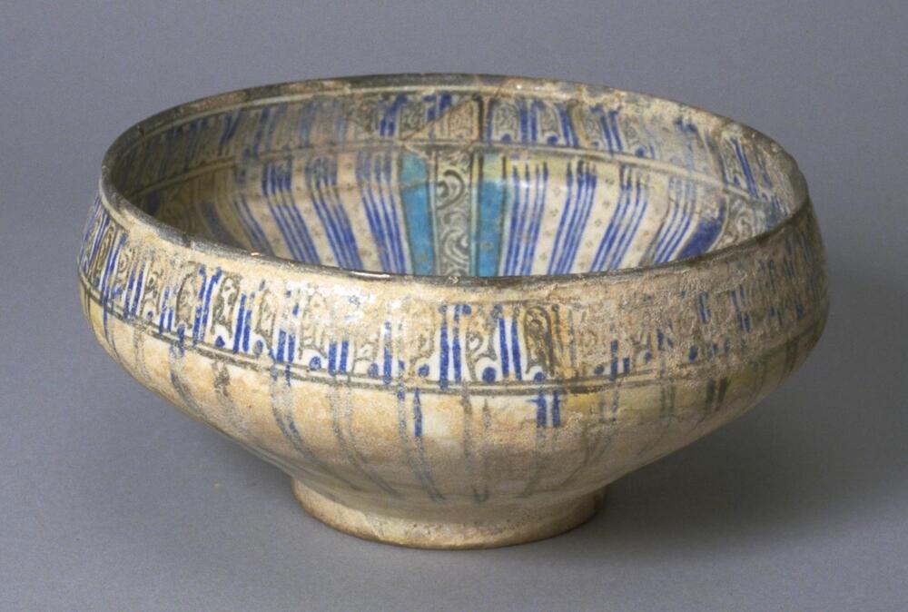 This glazed ceramic bowl with circular shape is typical of the Kashan style ceramicware from Iran. The interior features green foliage patterns, and a turquoise blue spotted donkey amidst blossoms within a blue medallion. The medallion has blue, turquoise blue, and green striped patterns. The exterior has blue and green floriated pseudo-Kufic designs<br /><br />
 