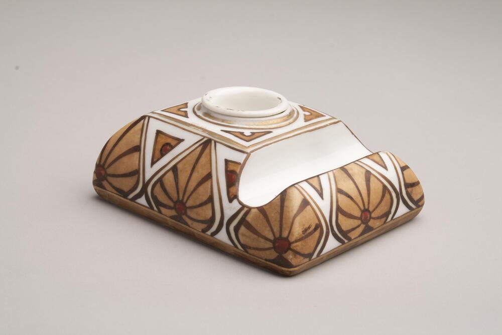 A porcelain inkwell with a rectangular body and a penstand on the one side; and it is decorated with drawings and patterns of brown leaves. There is no lid cover for the inkwell.