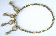 Belt with a string of brass and multi-colored beads and pendants in the form of large loops attached to a short rod with a small crotal bell at the end. 