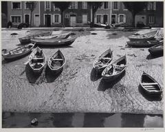 A horizontal image of boats docked on a shore. In the background are a row of townhouses.