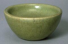 Porcelain double walled bowl, the outer wall has a gently rounded conical shape and the interior wall, a rounded base. The bowl has a direct rim and is covered in a green celadon glaze with craqueleur finish.  
