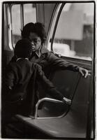 Woman and son on a bus, both holding onto the seat. Woman is facing the camera, boy is facing his mother.