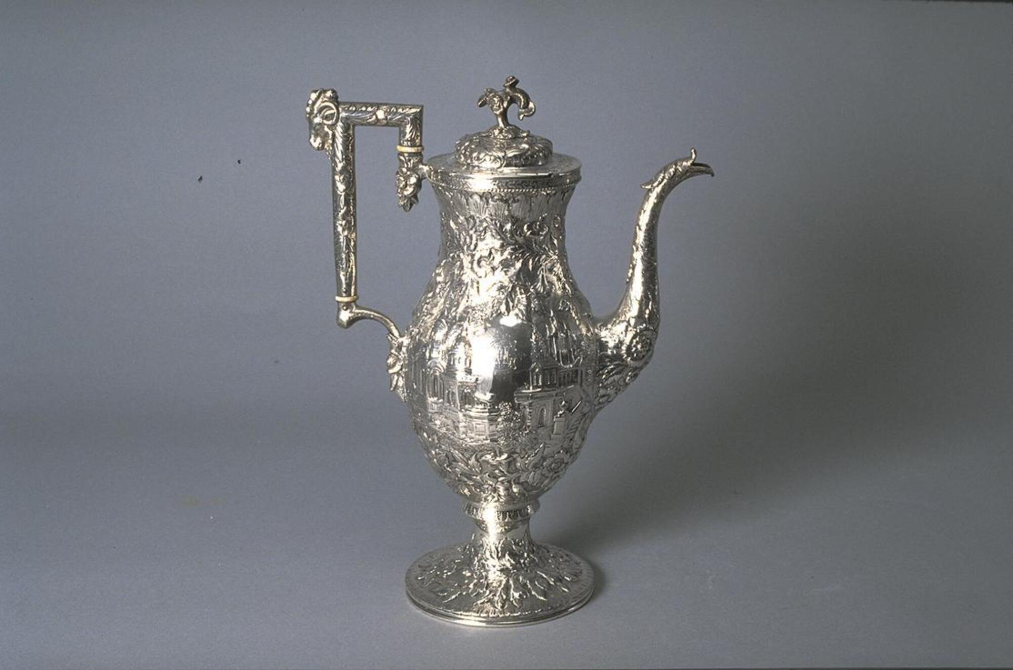 Tall, narrow silver pot with long spout, finial-topped lid, square handle and opulent repouss&eacute; decoration