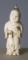 A carved ivory snuff bottle in the shape of a male child. He is standing and wearing a robe. On the top of his head is a stopper in the shape of hair in a high ponytail.