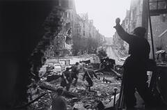 This image shows a view behind a group of soldiers running out of a destroyed building toward a war-ravaged street. 