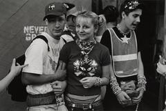 Two teenage boys and a teenage girl, both boys have on baseball caps, the girl has pigtails. They are all wearing a ton of bracelets.