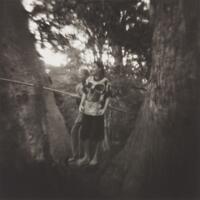 Two boys standing between trees, holding on to a large rope.