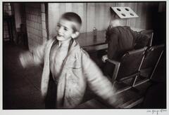 A little boy in an oversized coat twirling around, an older man trying to get out of a chair in the background.