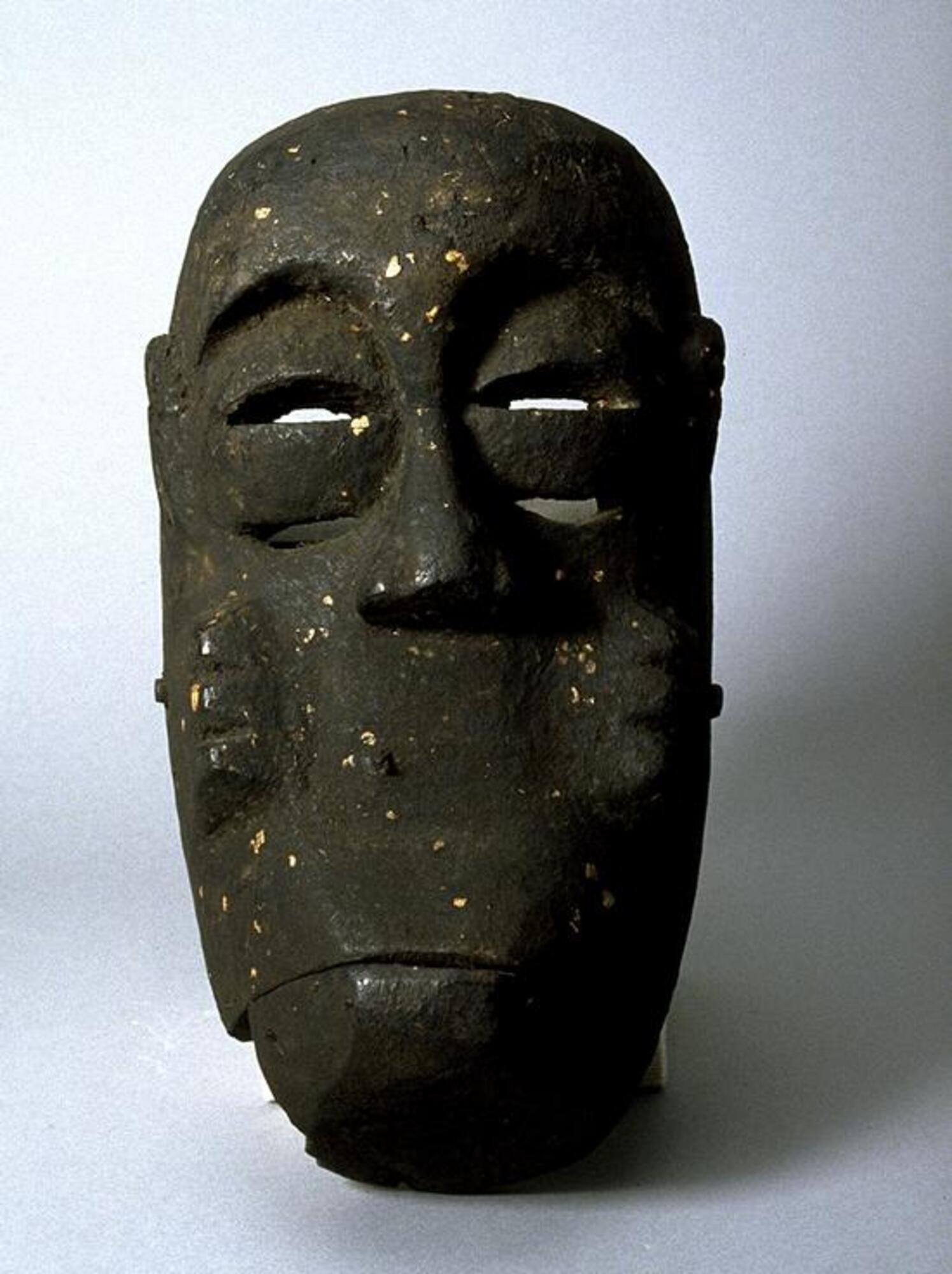 Large, ovoid mask with a dark patina. The forehead of the face is raised, sloping down to a short, broad nose. The eyes are formed by two cresent shapes separated by a rectangle. On each cheek are three raised marks in a vertical line. The mouth is closed and may be moveable. 