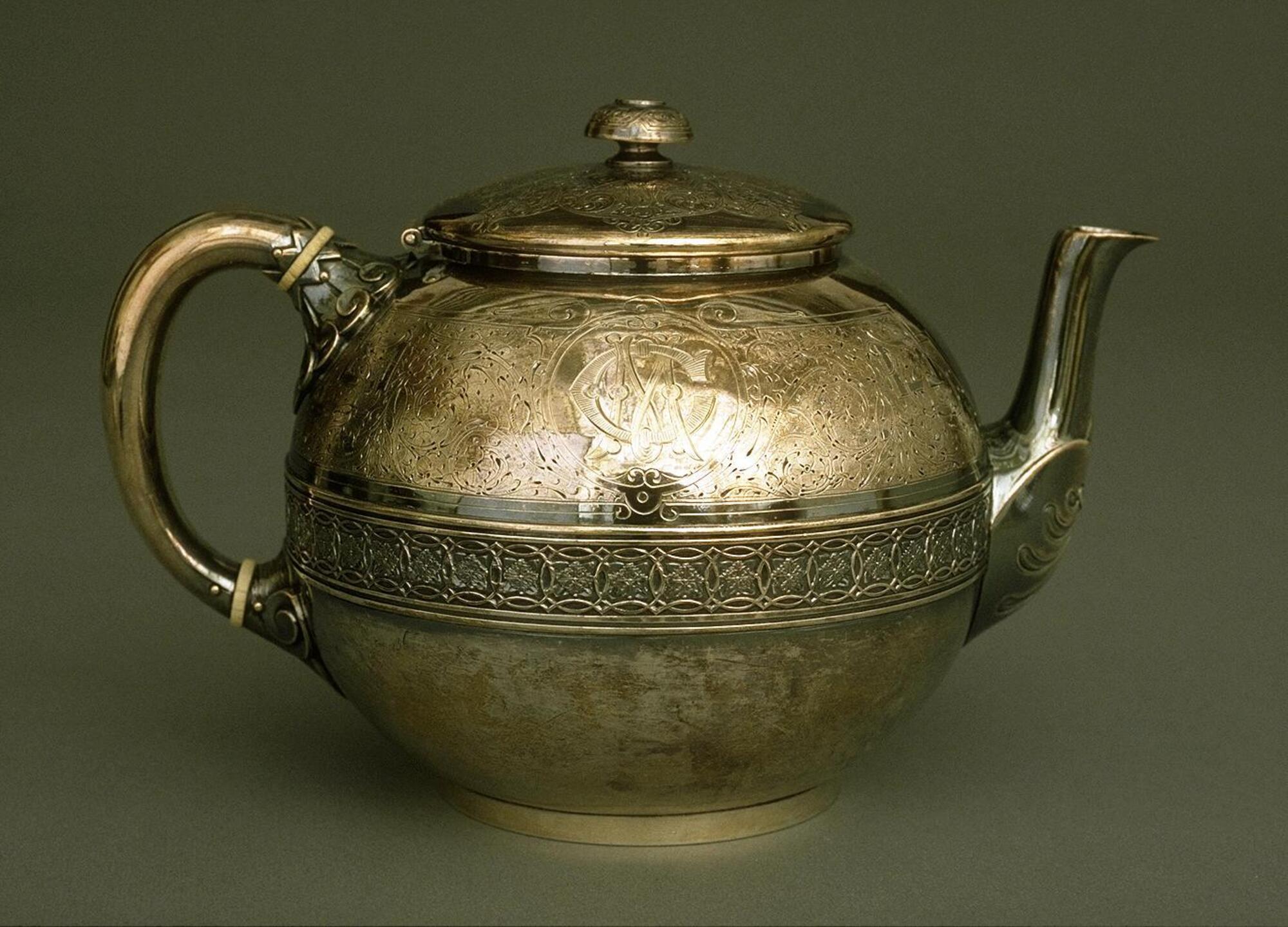 Silver teapot-shaped vessel with lid, handle, and spout and a band of decoration around center of the body