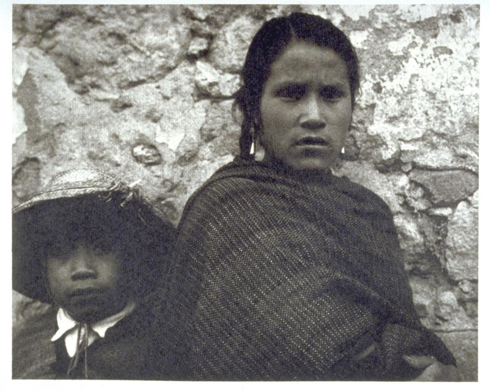 This is a photograph of a young woman and a young boy. They lean against a wall and look toward the camera.
