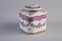 A porcelain white color inkwell has a rectangular body with round edges and a small lid. There are simple decorations and paintings of pink flowers on the inkwell.