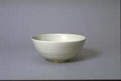 A porcelain hemispherical bowl with direct rim on a footring, the interior base is painted to depict a lion playing with a ball that looks like a coin, surrounded by a flowing ribbon. The bowl is covered in a clear glaze. 