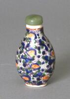 An oval snuff bottle with flower and leaf designs and blue, green, and orange curved lines, dots, and circles to accent the flower sand leaf designs. At the top is a green fluorite stopper.