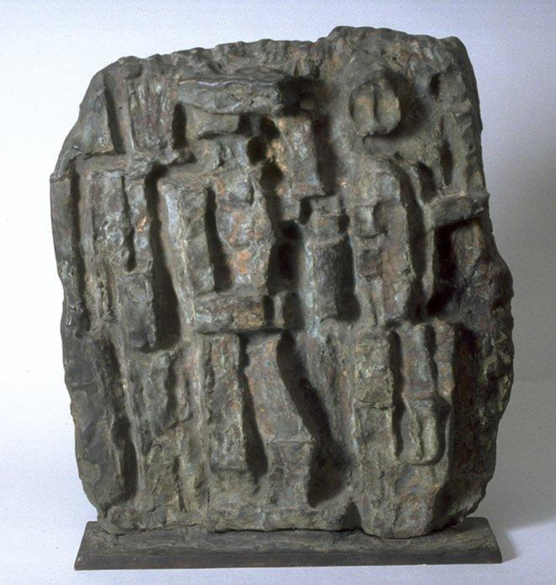 This relief sculpture shows three abstract human figures comprised of rectangular shapes set on a vertically orientated block. The figures and the background are textured and rough.