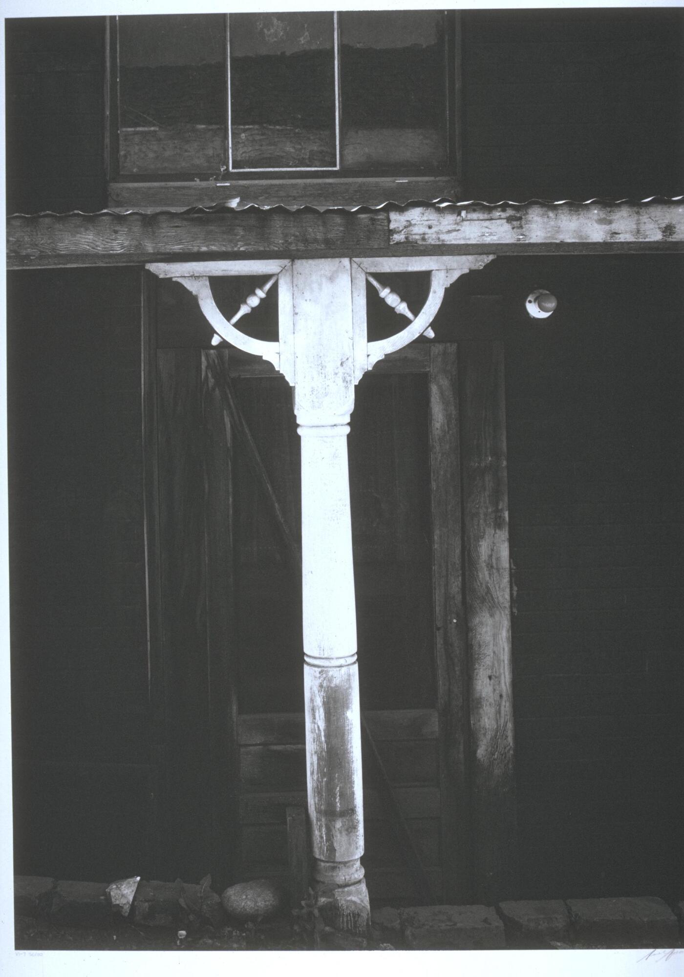 Photograph of a white painted post holding up the tin roof of a porch.