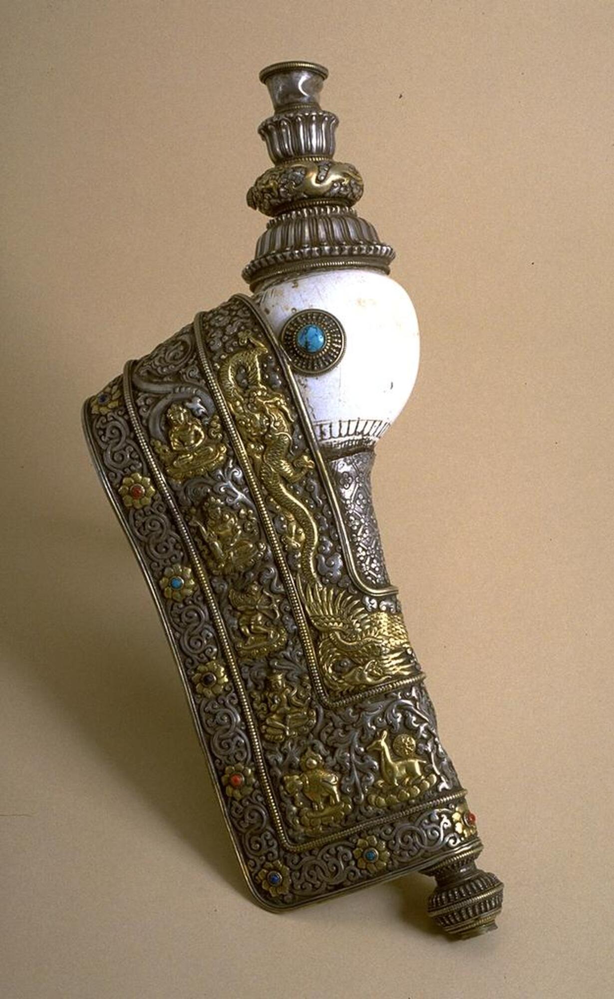An elaborately decorated conch shell trumpet, with extensions and a side chamber made from silver, inlaid with other precious metals and semi-precious stones of turquoise, lapiz lazuli, and mountain coral.