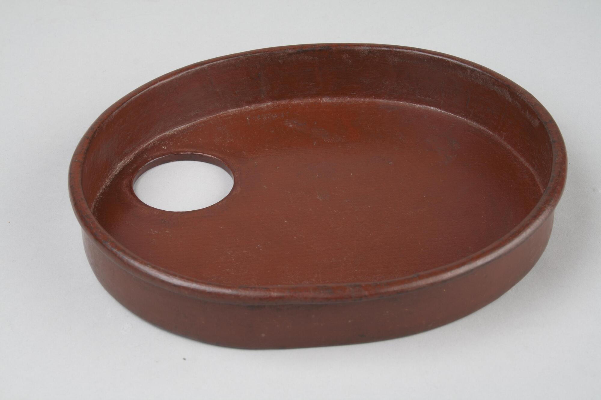Oval wooden tray with one inch lip and rounded edge. There is a two inch hole to allow room for the whisk. This is a part of a portable tea set.