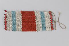 Beaded jewlery with a rectangular piece in striped design. One wide red stripe in the middle with two blue stripes on either end on background of white. Row of large beads on either end, one string coming off end, white tag attached.