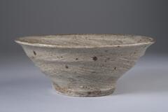 Small ceramic bowl with narrow bottom and wide top. Brown-grey color with dark brown speckles. Pattern of brush strokes spiraling down into the center of the bowl.