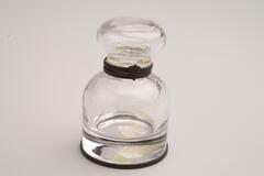 This is a clear glass inkwell with a metal rim around the neck and base. The body and stopper have a rounded shape.