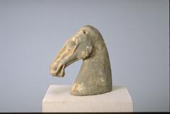 A gray earthenware head from a horse sculpture. Its muscular neck holds its narrow head high; it is vividly sculpted to show the musculature of the horse's face with flaring nostrils and open mouth showing its tongue within.  There is loss of the ears.  The head has traces of red and white mineral pigment. 