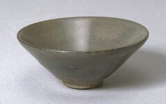 A conical bowl on a tall straight foot ring, covered in an underfired dark brown-black glaze which appears dark mottled gray, with a semi-matte surface instead of a glossy one. 