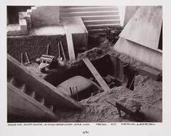 Car under excavation under stairs. There is a wheelbarrow and other excavation equipment.