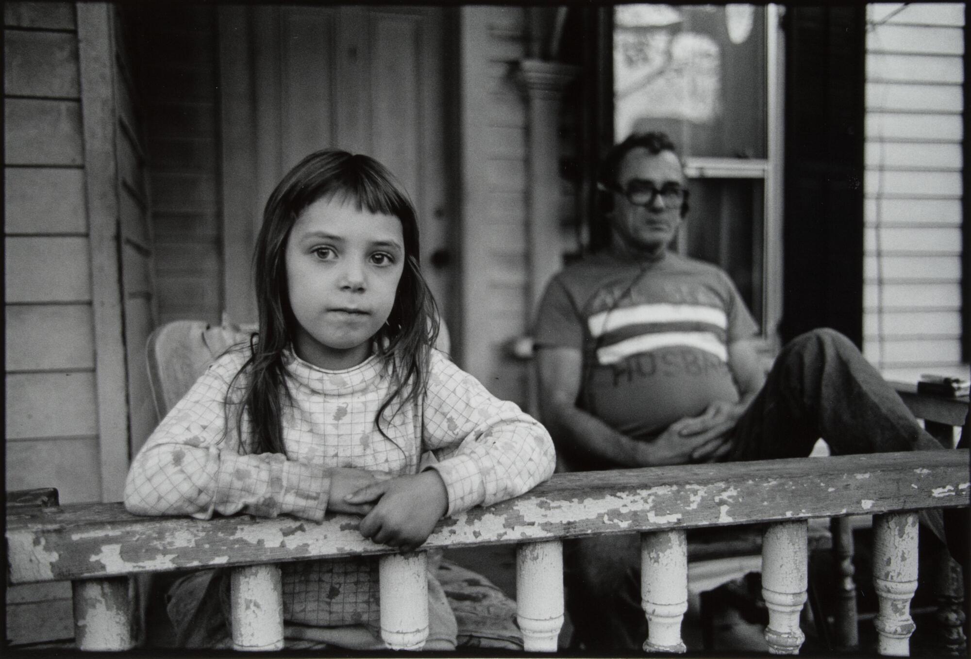 A girl and an older man in glasses sitting on a front porch.
