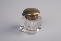 A small, square glass inkwell with a brass lid.