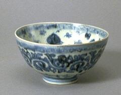 A porcelain hemispherical bowl on a footring with bands of underglaze cobalt blue floral scroll meander around the exterior body and around the interior rim. The interior has a larger floral pattern against a smaller floral background pattern and is covered in a clear glaze.