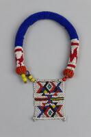 Beaded bracelet with rounded main piece in blue beads with end detail in white and red beads. Beaded rectangular piece at one end with geometric detail in white, blue, red, black and yellow. Loop closure with larger yellow beads, white tag attached.
