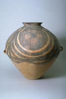 A light reddish-buff earthenware <em>guan </em>罐 jar with a wide globular upper body and conical lower body on a flat base, and a short narrow everted neck with direct rim. There are two diametrically opposed lug handles at the waist. The upper half of the body is painted with black and red pigments to depict four whirls of concentric circles, each containing a roundel of a checkerboard pattern created from vertical and horizontally striped squares alternating with squares containing a network pattern. The four circular motifs are confined between solid band borders, with a garland border below. Around the neck is a thick, wide zigzag pattern.