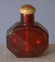 A red octogonal glass snuff bottle with carnelian stopper set in a horn collar.
