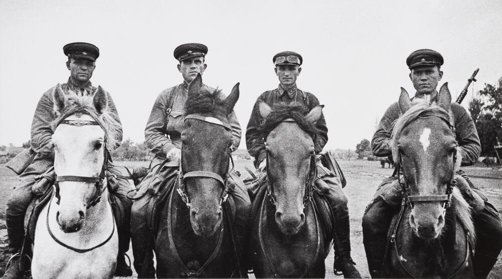 Four men in military uniforms on horseback look out directly at the viewer.