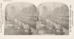 This black and white stereoscopic image features two images showing women washing laundry along the bank of a narrow river or canal. There are trees on the opposite bank and buildings in the distance. It is surrounded by the text: Sample Set No. 2; C. H. Graves, Publisher and Gen’l Manager; 7237 Wash-day in Italy.  <br />